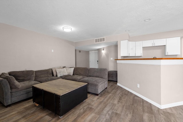 living area featuring visible vents, a textured ceiling, baseboards, and wood finished floors