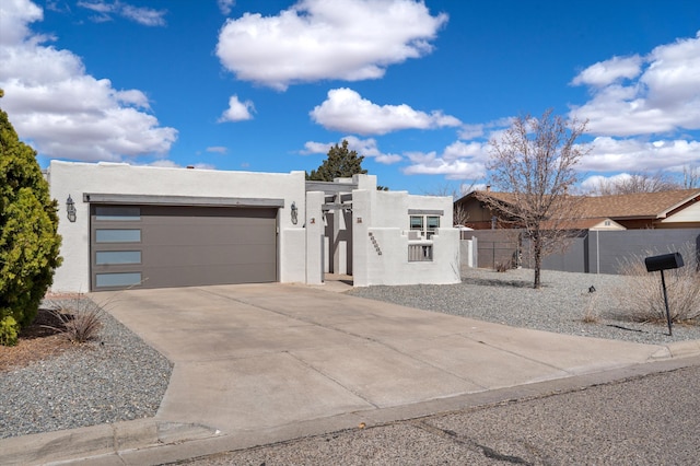 pueblo revival-style home featuring a fenced front yard, stucco siding, driveway, and a garage