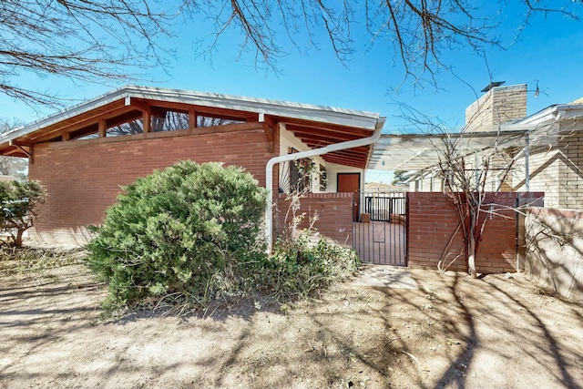 view of property exterior with fence, brick siding, and a gate