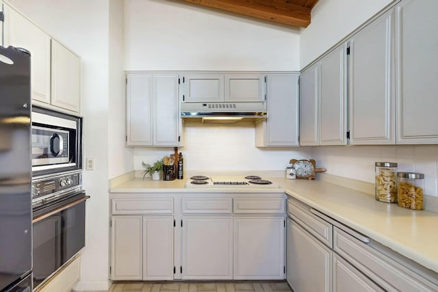 kitchen with under cabinet range hood, black oven, stainless steel microwave, freestanding refrigerator, and white electric stovetop