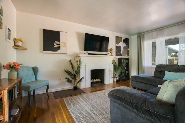 living area with baseboards, a brick fireplace, and wood finished floors