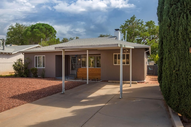 rear view of property with stucco siding, roof with shingles, and fence