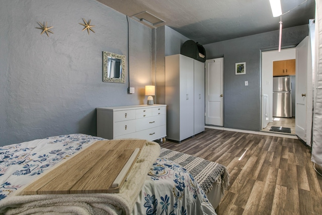 bedroom featuring dark wood-type flooring, a textured wall, and freestanding refrigerator