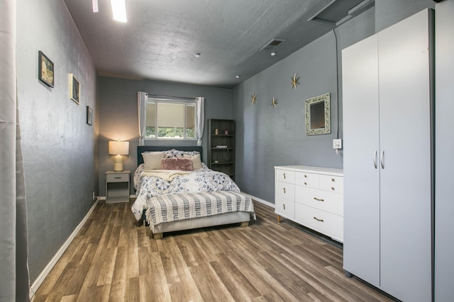 bedroom with visible vents, baseboards, wood finished floors, and a textured wall