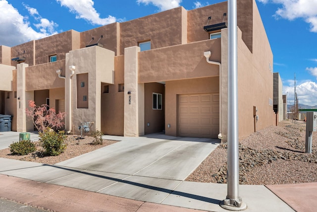 pueblo-style house with a garage, driveway, and stucco siding