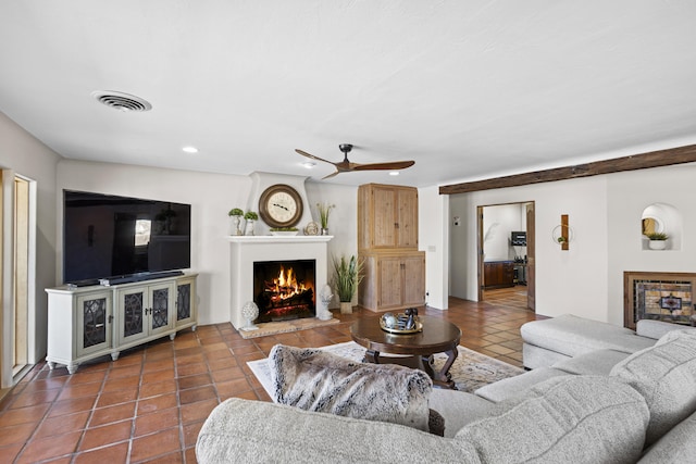 living area featuring tile patterned flooring, visible vents, a warm lit fireplace, and ceiling fan