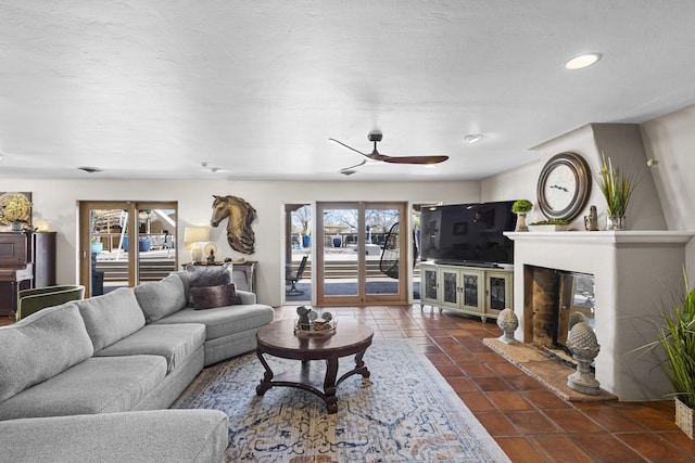 living room featuring a glass covered fireplace, a ceiling fan, and dark tile patterned flooring