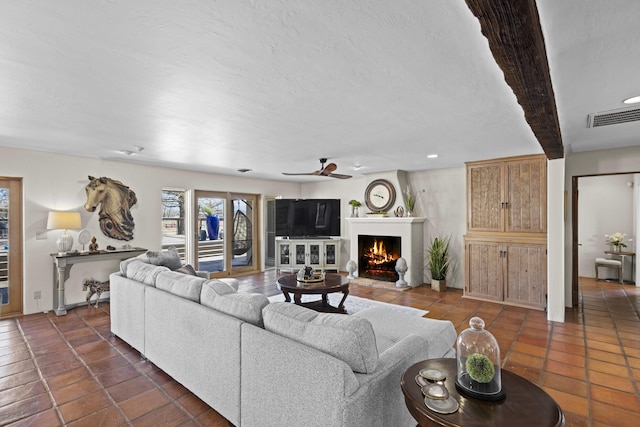 living room featuring visible vents, a lit fireplace, a textured ceiling, a ceiling fan, and dark tile patterned flooring