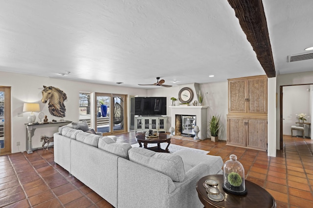 living area featuring a glass covered fireplace, dark tile patterned flooring, a ceiling fan, and visible vents