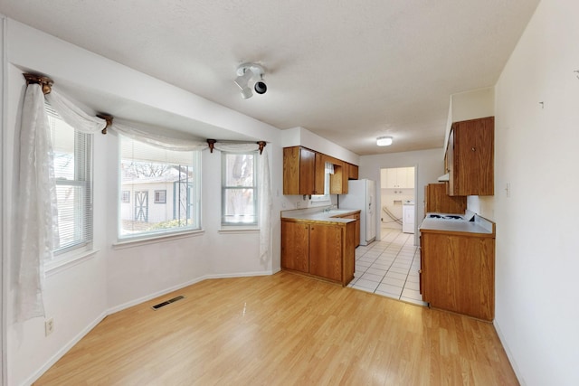 kitchen with visible vents, brown cabinets, freestanding refrigerator, light wood finished floors, and light countertops