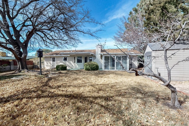 back of house featuring stucco siding, an outbuilding, a lawn, and a sunroom