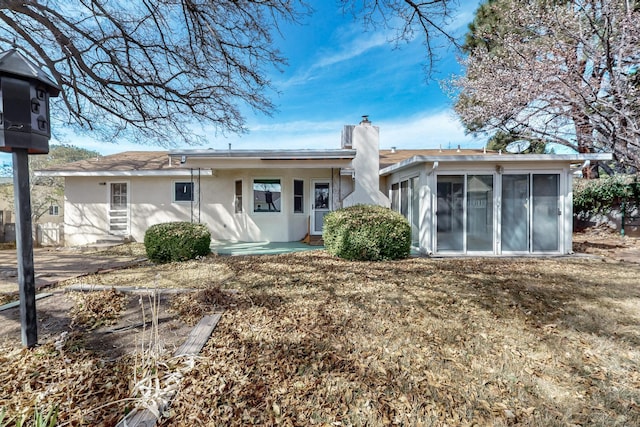 back of house featuring a chimney, a sunroom, and stucco siding