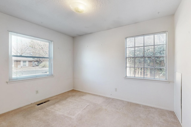 unfurnished room with visible vents, plenty of natural light, and light colored carpet