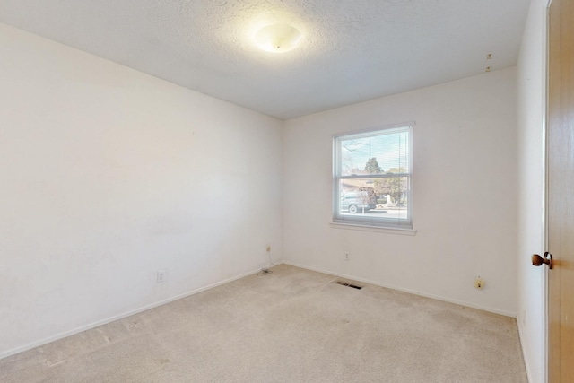 empty room featuring visible vents, baseboards, light colored carpet, and a textured ceiling