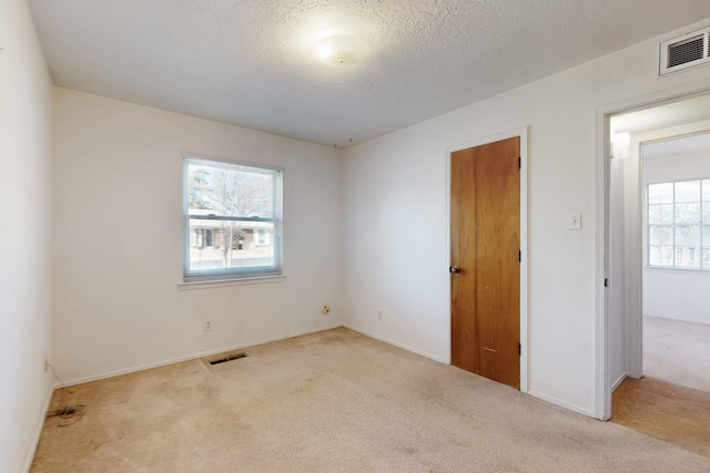 carpeted spare room featuring visible vents, a textured ceiling, and baseboards