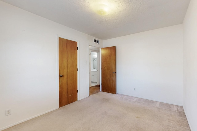 carpeted spare room with visible vents and a textured ceiling