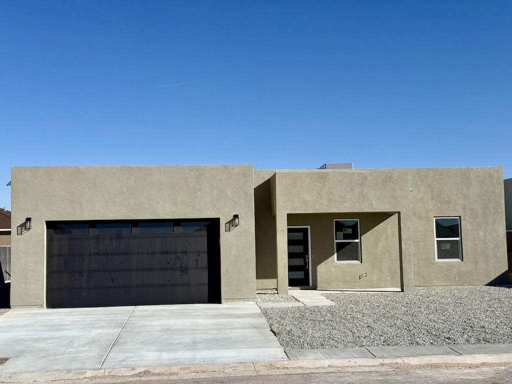 pueblo-style house with stucco siding, an attached garage, and concrete driveway