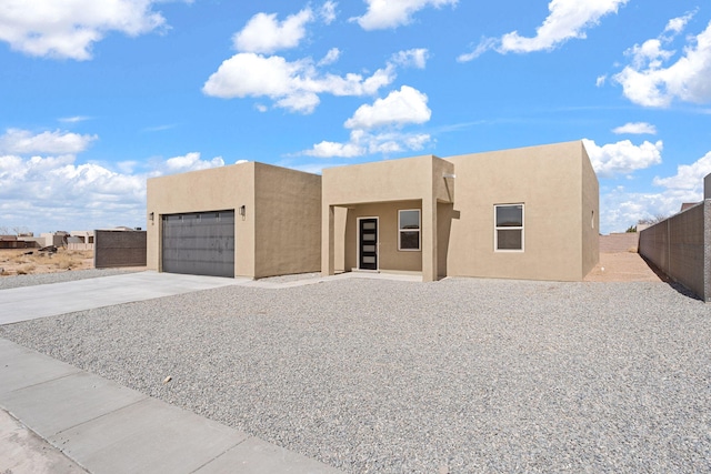 pueblo-style home featuring stucco siding, concrete driveway, an attached garage, and fence