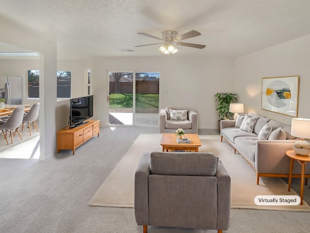 living room with a ceiling fan, visible vents, carpet floors, and a textured ceiling