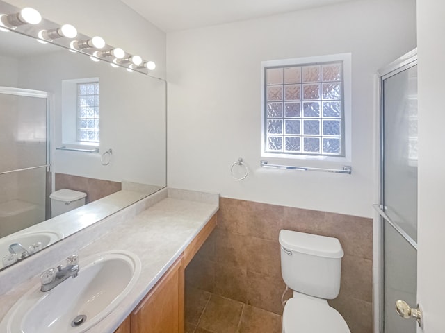 bathroom featuring tile walls, a wainscoted wall, toilet, a shower with shower door, and vanity