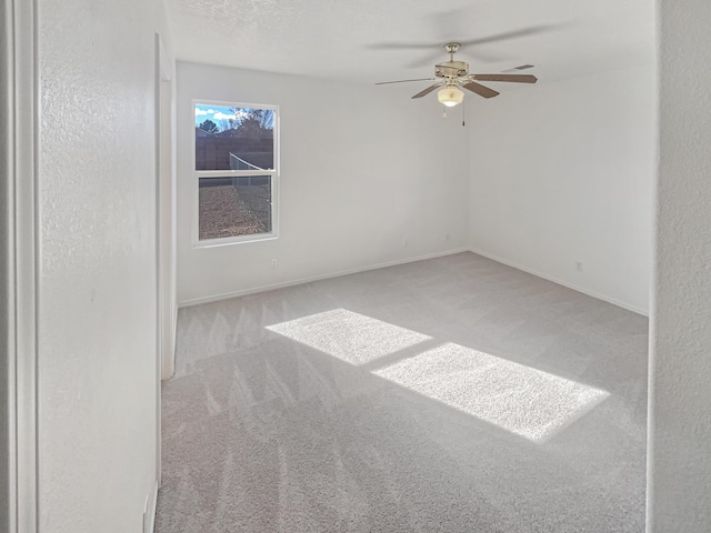 empty room with a textured ceiling, carpet, baseboards, and ceiling fan