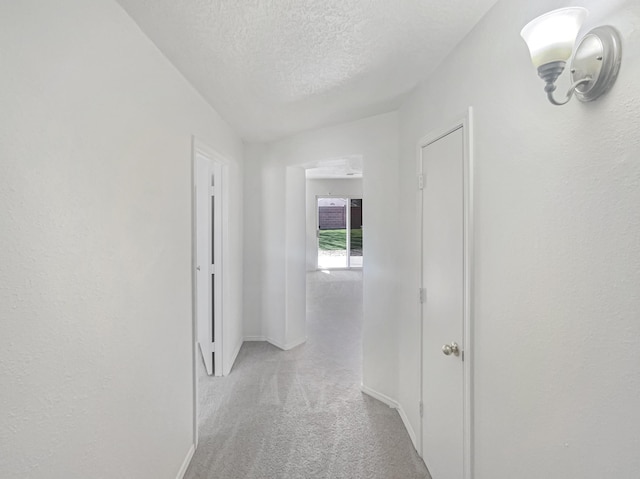 hallway with baseboards, carpet floors, and a textured ceiling