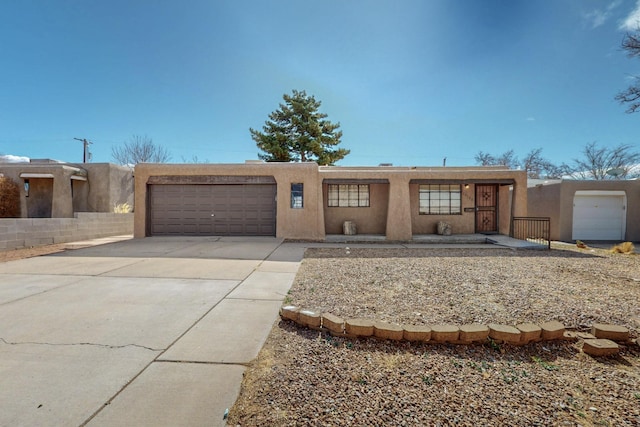 pueblo-style house featuring concrete driveway, an attached garage, and stucco siding