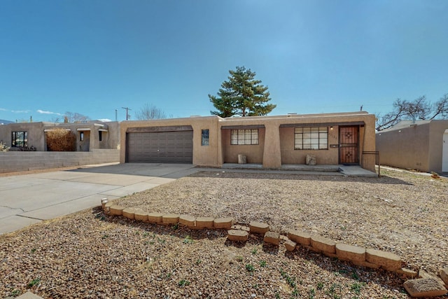 pueblo revival-style home featuring concrete driveway, an attached garage, and stucco siding