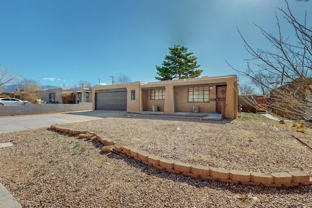 pueblo revival-style home featuring a garage, driveway, and stucco siding