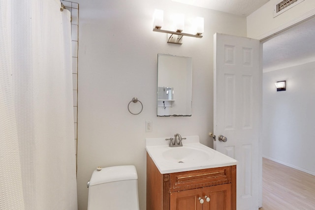 bathroom with toilet, vanity, baseboards, and wood finished floors