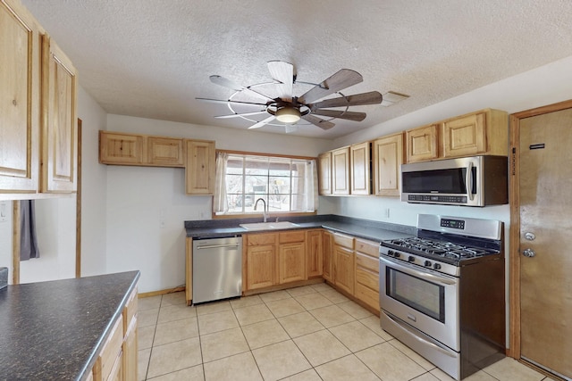 kitchen with dark countertops, light brown cabinetry, appliances with stainless steel finishes, a ceiling fan, and a sink