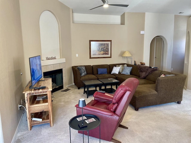 living area featuring a ceiling fan, arched walkways, carpet, a fireplace, and baseboards