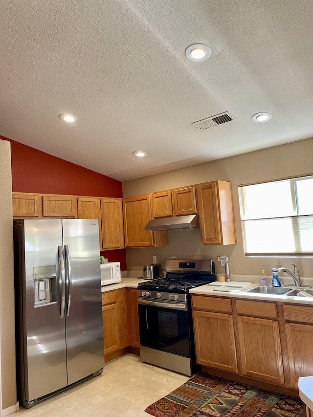 kitchen featuring visible vents, a sink, under cabinet range hood, stainless steel appliances, and light countertops