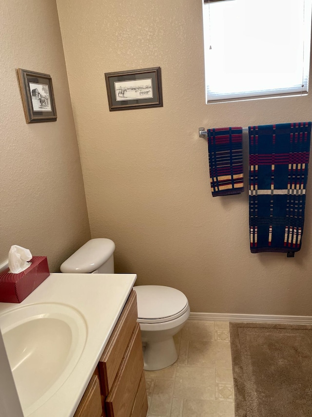 half bathroom featuring baseboards, toilet, and vanity