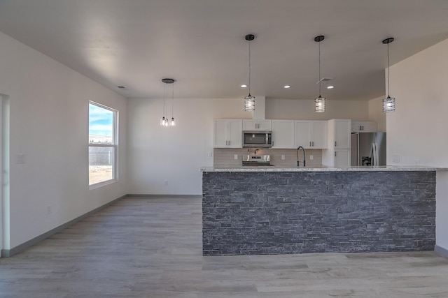 kitchen with a sink, light wood-style floors, white cabinetry, appliances with stainless steel finishes, and light stone countertops
