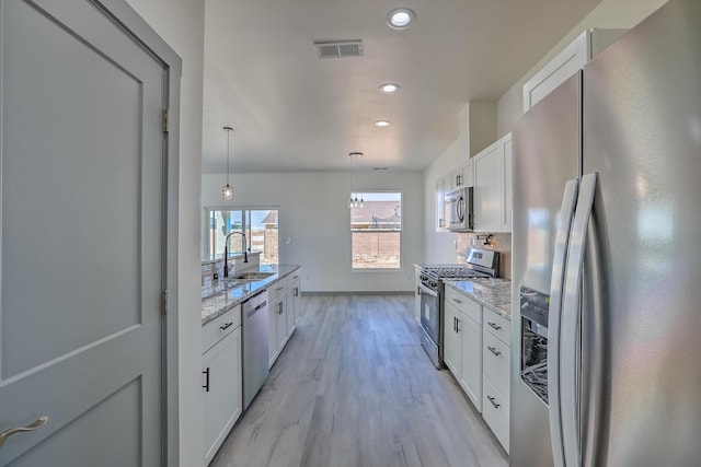 kitchen with recessed lighting, white cabinets, light wood finished floors, a sink, and appliances with stainless steel finishes