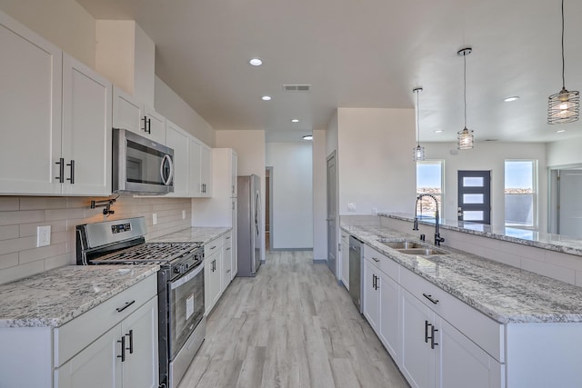 kitchen with a sink, decorative backsplash, a peninsula, appliances with stainless steel finishes, and visible vents