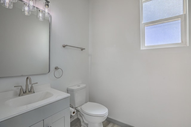 half bath with baseboards, toilet, and vanity