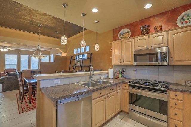 kitchen with a peninsula, a sink, stainless steel appliances, dark countertops, and backsplash