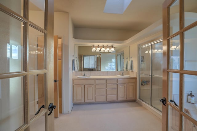 full bathroom with double vanity, a shower with shower door, a skylight, and a sink