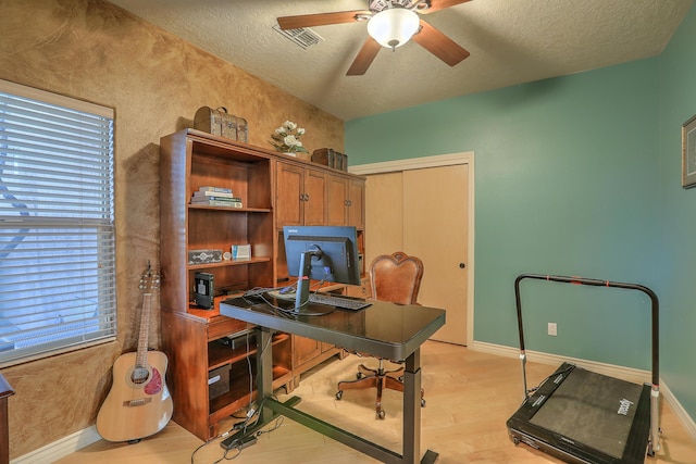 office area with a ceiling fan, visible vents, baseboards, light wood-style floors, and a textured ceiling