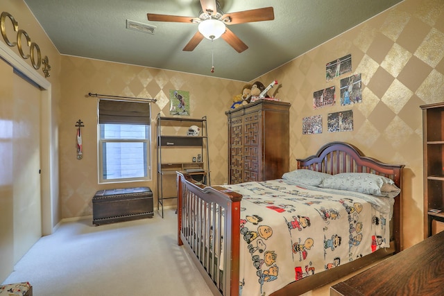 carpeted bedroom with visible vents, a textured ceiling, a ceiling fan, and wallpapered walls