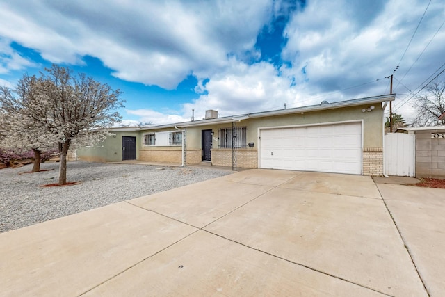 single story home with brick siding, concrete driveway, stucco siding, a garage, and a gate