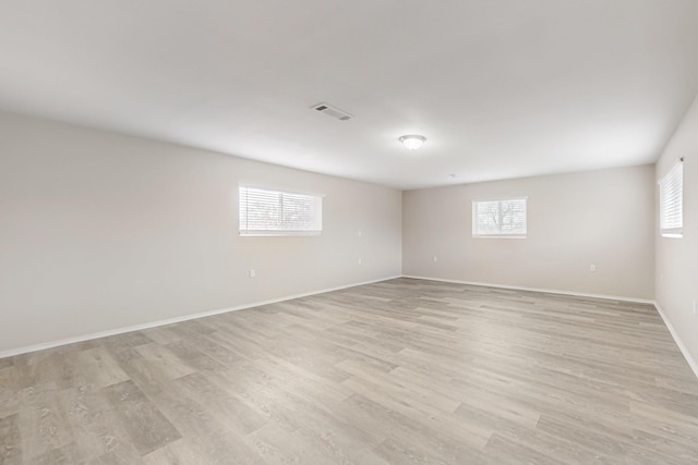 spare room with visible vents, light wood-type flooring, a wealth of natural light, and baseboards