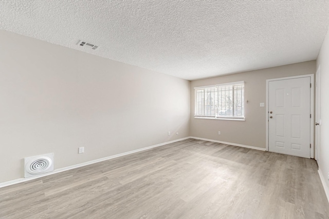 spare room featuring light wood finished floors, visible vents, a textured ceiling, and baseboards