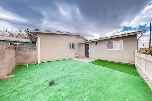 rear view of house with stucco siding, a yard, and a fenced backyard