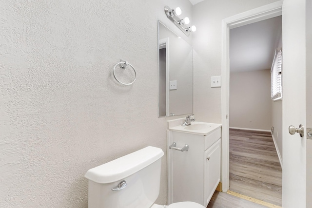 half bathroom featuring vanity, toilet, wood finished floors, and baseboards