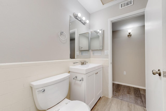 half bathroom featuring visible vents, a wainscoted wall, toilet, wood finished floors, and vanity