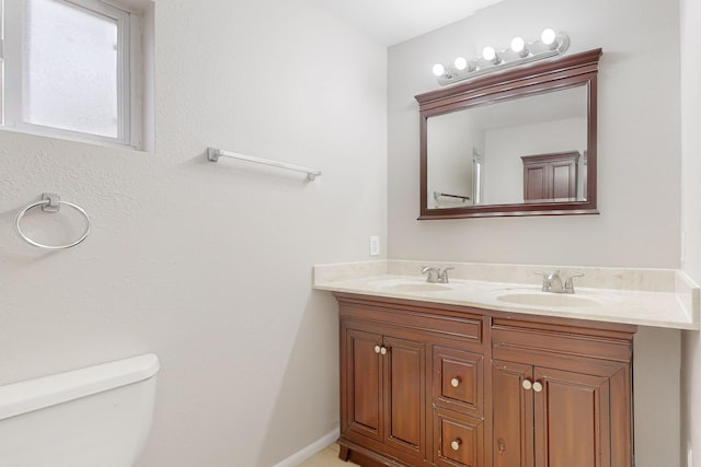 bathroom with double vanity, toilet, baseboards, and a sink