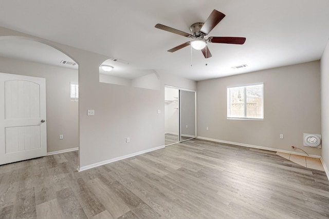 unfurnished bedroom with visible vents, arched walkways, light wood finished floors, baseboards, and ceiling fan